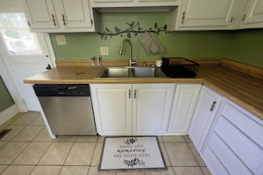 A kitchen with white cabinets, a stainless steel dishwasher, a sink, and a tiled floor. - Build memories in WNC! (Brevard)