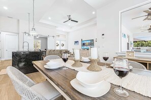 Ein stilvoller Essbereich mit einem langen Holztisch, der für eine Mahlzeit gedeckt ist, eine Küche mit einer schwarzen Marmorarbeitsplatte und ein Wohnzimmer mit einer Couch und einem Fernseher.