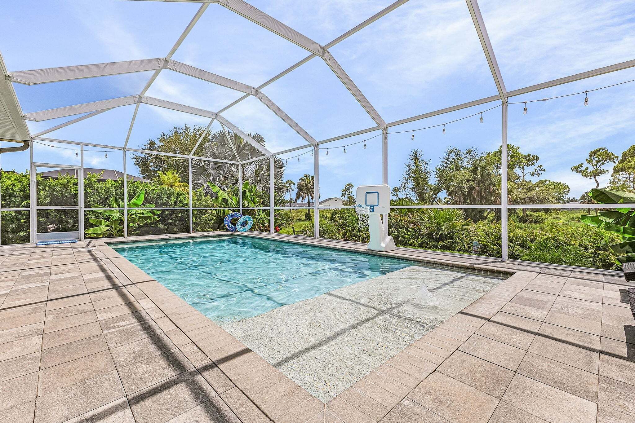 A covered swimming pool with a clear blue water surface, surrounded by a white metal frame structure.