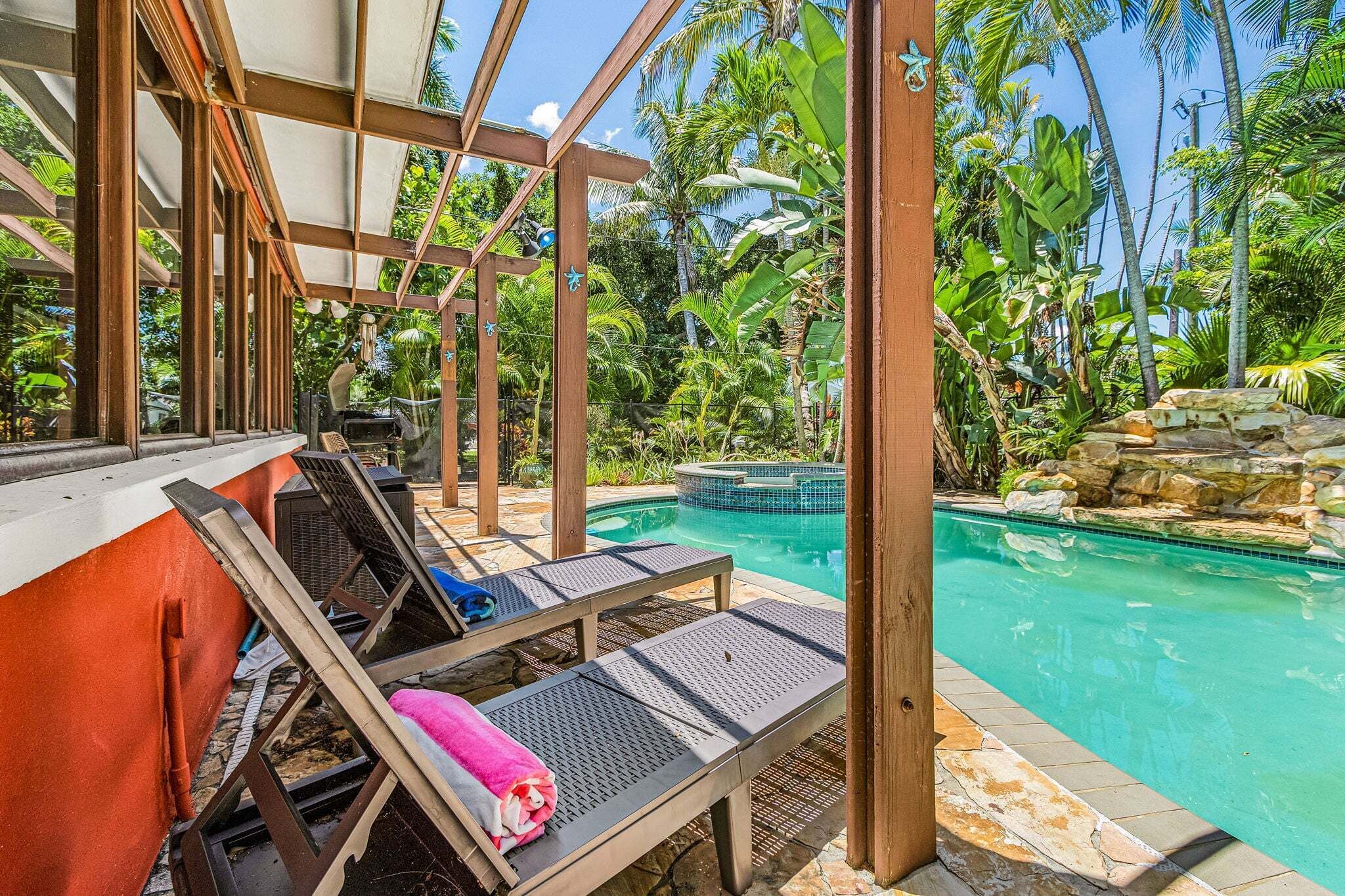 Zona junto a la piscina con sillones de descanso y vista despejada a una piscina rodeada de vegetación tropical.