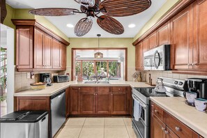 A kitchen with wooden cabinets, a stainless steel refrigerator, a microwave, and a stove. - Tropical Retreat with Heated Pool, Spa & Tiki Bar - Coastal Paradise Getaway - Roelens (Cape Coral)