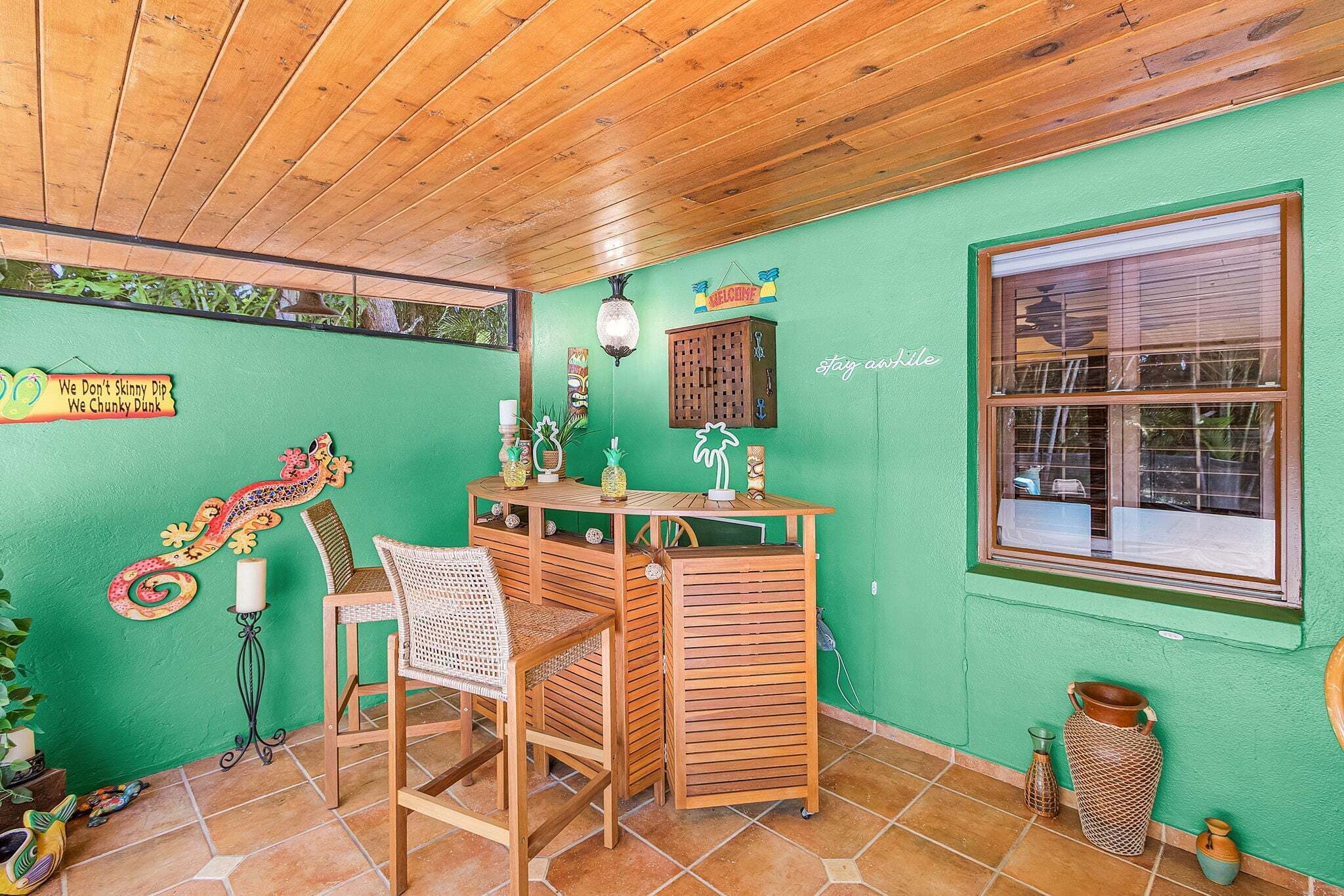 Une pièce avec un plafond en bois, un mur vert, un bureau en bois avec une chaise et une fenêtre.