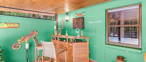 A room with a wooden ceiling, a green wall, a wooden desk with a chair, and a window.