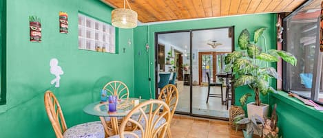 A dining area with a round table and chairs, a wooden ceiling, and a green wall with decorative elements.