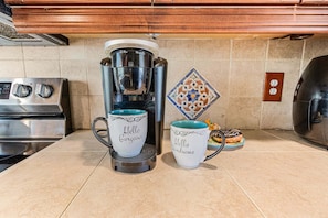 A kitchen with a coffee maker, two mugs, a decorative tile, and a donut on a plate. - Tropical Retreat with Heated Pool, Spa & Tiki Bar - Coastal Paradise Getaway - Roelens (Cape Coral)