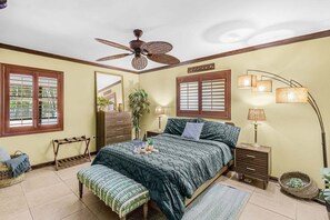 A bedroom with a bed, bedside tables, a ceiling fan, a mirror, and a window with blinds. - Tropical Retreat with Heated Pool, Spa & Tiki Bar - Coastal Paradise Getaway - Roelens (Cape Coral)
