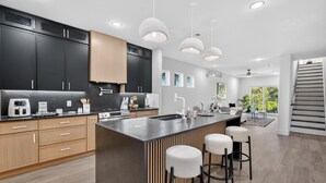 Uma cozinha moderna com armários escuros, uma ilha central, banquetas altas e iluminação pendente.
