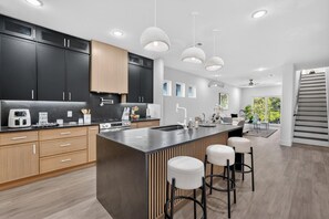 A modern kitchen with dark cabinets, a central island, bar stools, and pendant lighting. - 3-bedroom brand new modern house in  Dallas with cool AC for relaxing stay (Dallas)