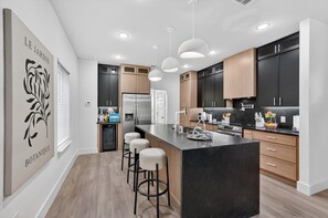 Una cocina moderna con una isla central, luces colgantes y un refrigerador negro.