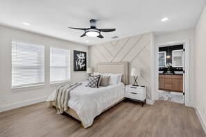 A bedroom with a bed, bedside tables, a ceiling fan, and a view into the bathroom. - 3-bedroom brand new modern house in  Dallas with cool AC for relaxing stay (Dallas)
