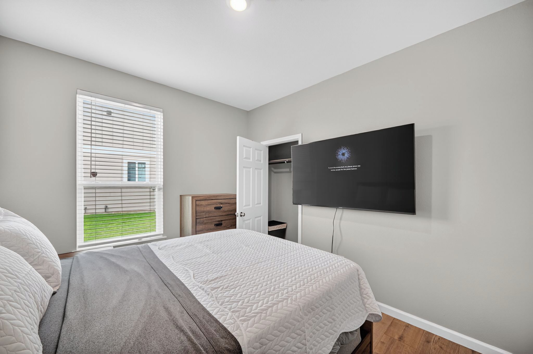 Een slaapkamer met een bed, een aan de muur bevestigde televisie, een raam met zonwering en een deur.