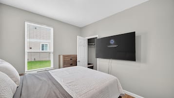Een slaapkamer met een bed, een aan de muur bevestigde televisie, een raam met zonwering en een deur.