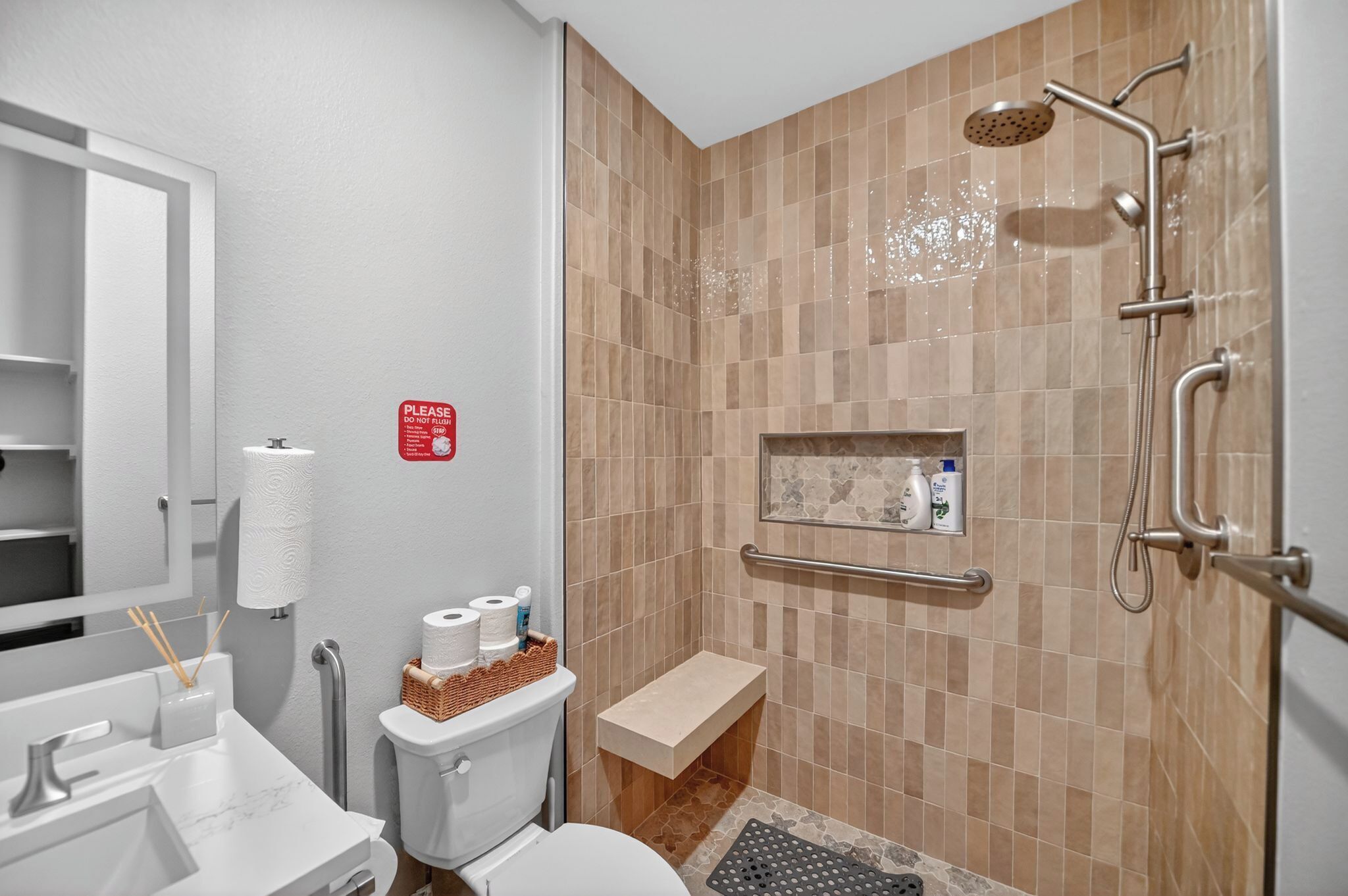 A bathroom with a shower, toilet, sink, and a handrail.