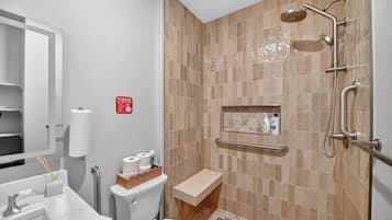 A bathroom with a shower, toilet, sink, and a handrail.