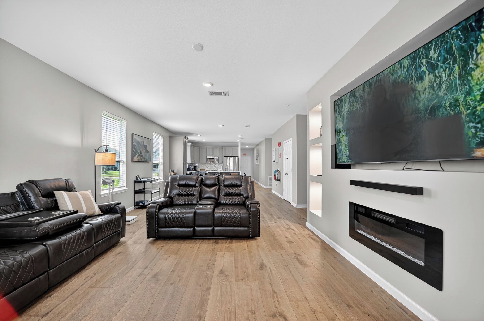A modern living room with a leather sofa, a fireplace, and a large flat-screen TV mounted on the wall.