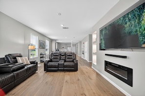 A modern living room with a leather sofa, a fireplace, and a large flat-screen TV mounted on the wall. - Modern Comfort House ADA Friendly Spacious & Family Ready (Hockley)