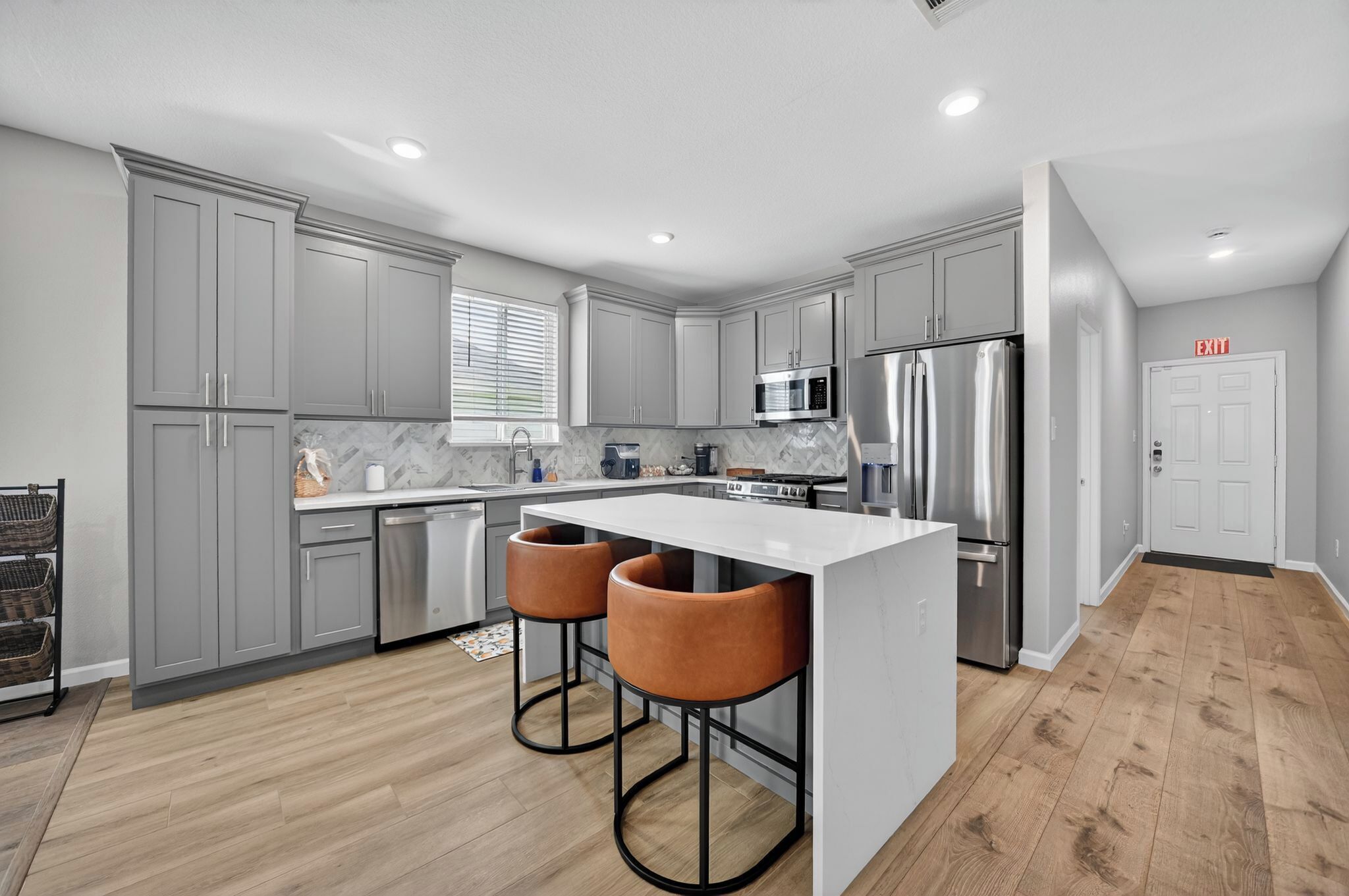 A modern kitchen with grey cabinets, stainless steel appliances, and a central island with bar stools.