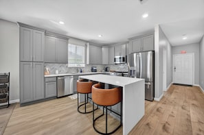 A modern kitchen with grey cabinets, stainless steel appliances, and a central island with bar stools. - Modern Comfort House ADA Friendly Spacious & Family Ready (Hockley)