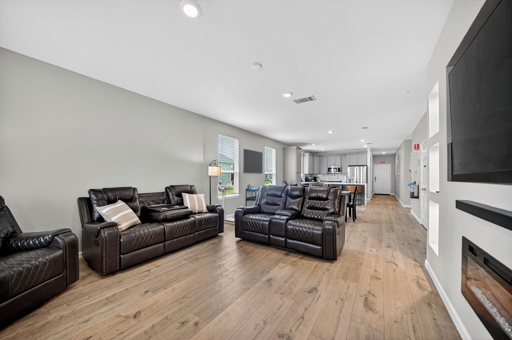 A modern living room with leather sofas, a dining area, and a kitchen in the background.
