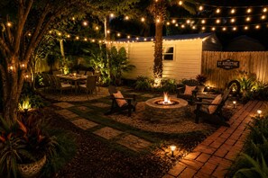 An outdoor patio area with a fire pit, seating, string lights, and a wooden fence. - Old City Marsh View Retreat Pets Welcome (St. Augustine)