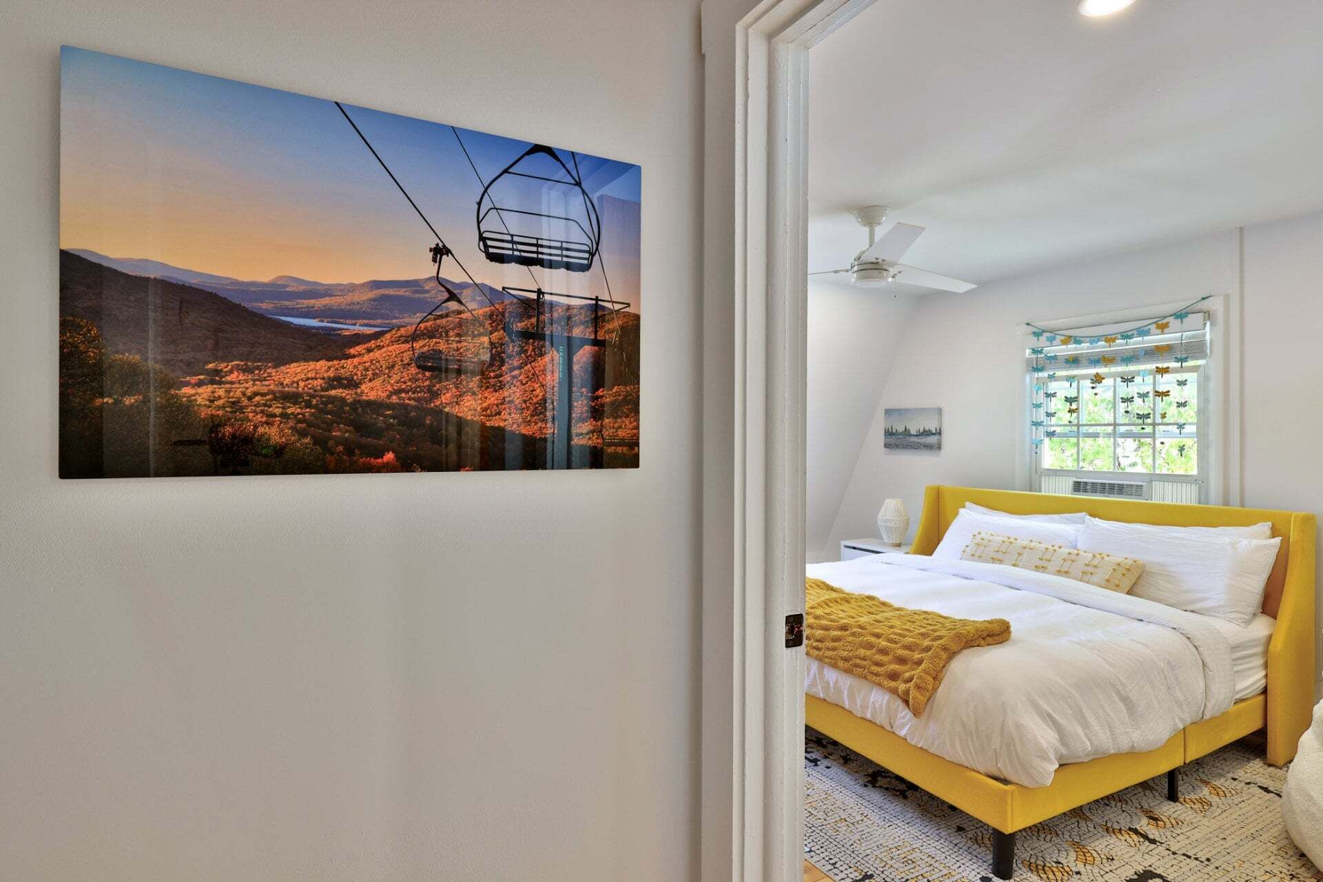 Ein Schlafzimmer mit einem Bett, einem Fenster mit Vorhängen, einem Deckenventilator und einem Wandbild.