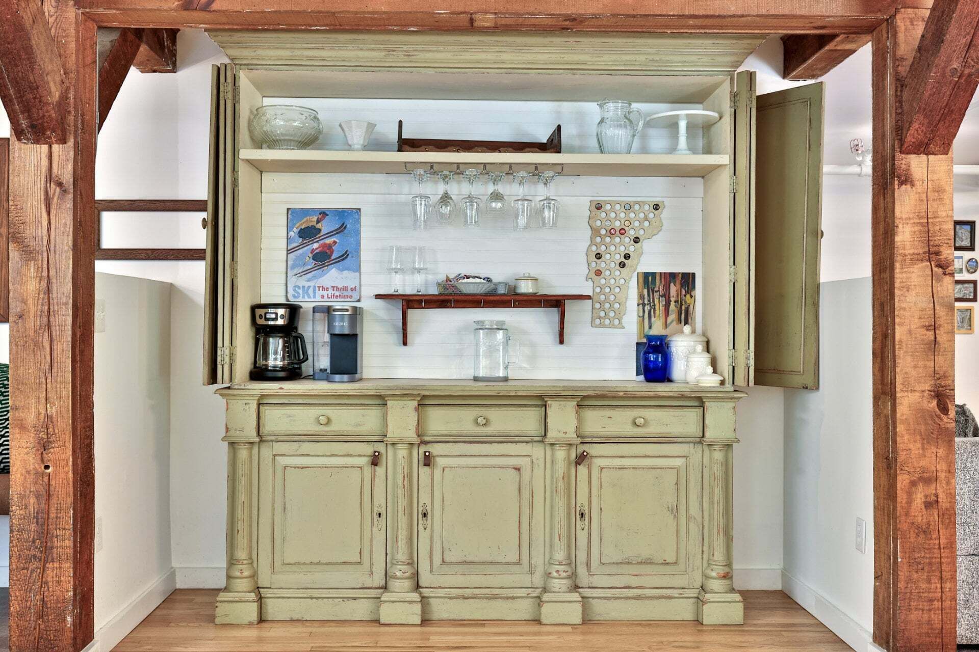 A vintage-style kitchen with a wooden counter, a coffee maker, a kettle, and a shelf with glassware.