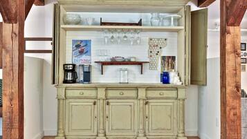 A vintage-style kitchen with a wooden counter, a coffee maker, a kettle, and a shelf with glassware.