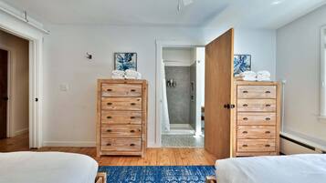 A bedroom with two beds, wooden dressers, a shower, and a blue patterned rug.