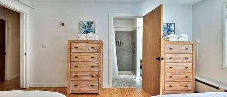 Quarto com duas camas, cómoda de madeira, chuveiro e tapete azul estampado.