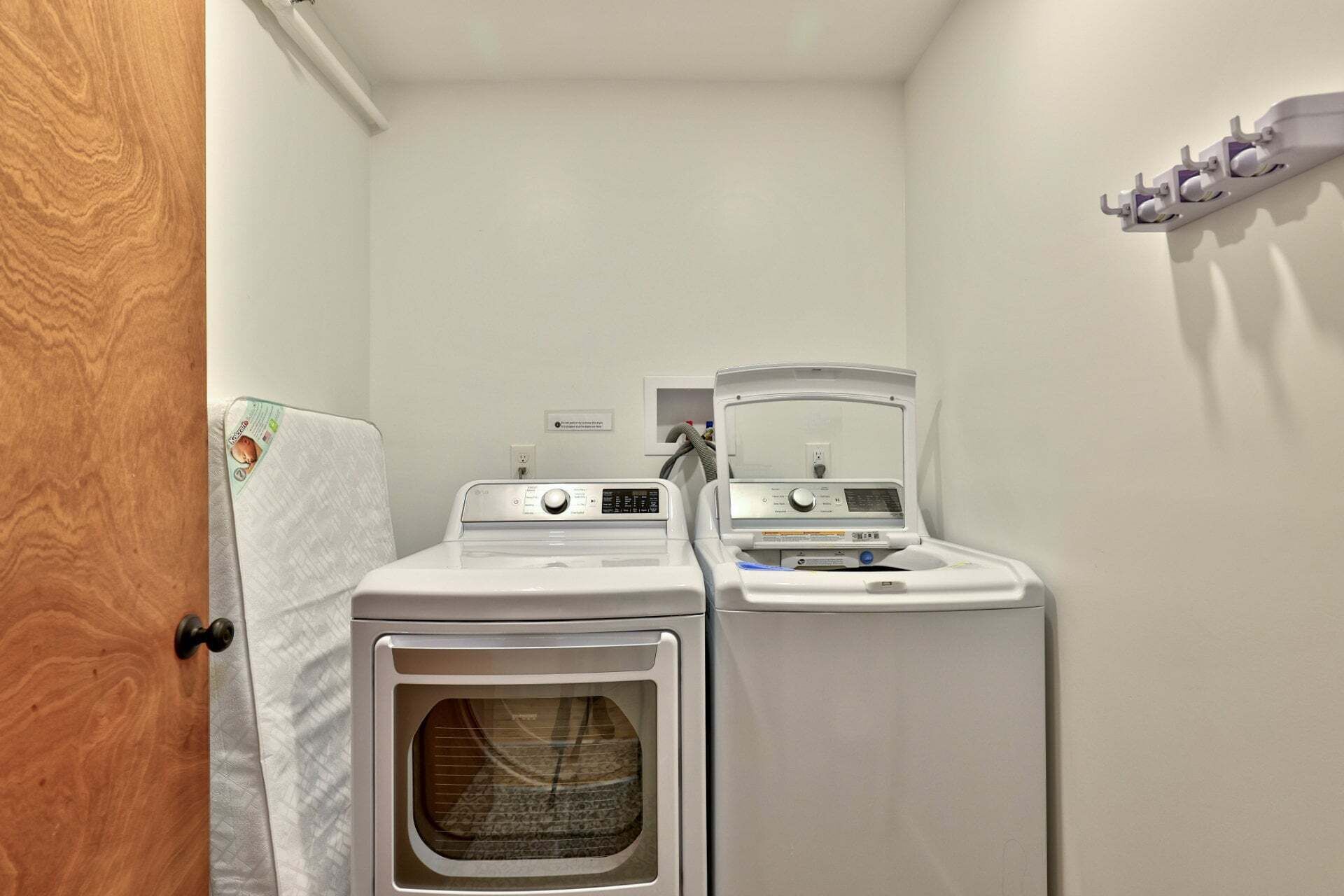 A laundry room with two stacked washers and dryers, a wooden door, and a towel rack on the wall.