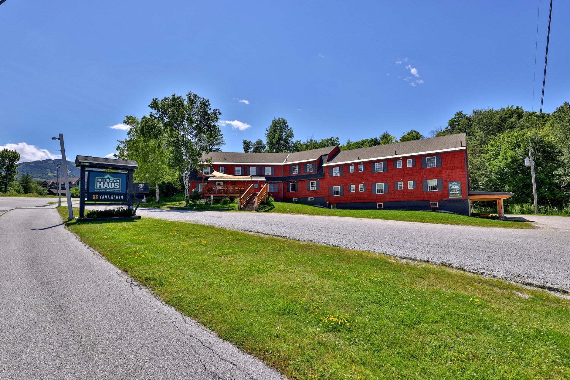 A red building with a covered outdoor seating area, a signboard, and a gravel path leading to it.