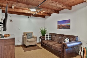 Ein Wohnzimmer mit braunem Ledersofa, einem beigen Sessel, einem Couchtisch und einem Gemälde an der Wand.
