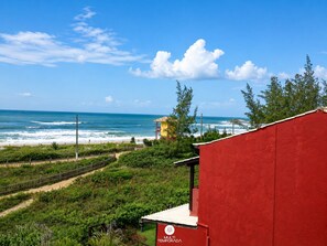 Edificio rojo con un letrero que dice 'MULTI TEMPORADA' frente a una playa con olas y cielo despejado.
