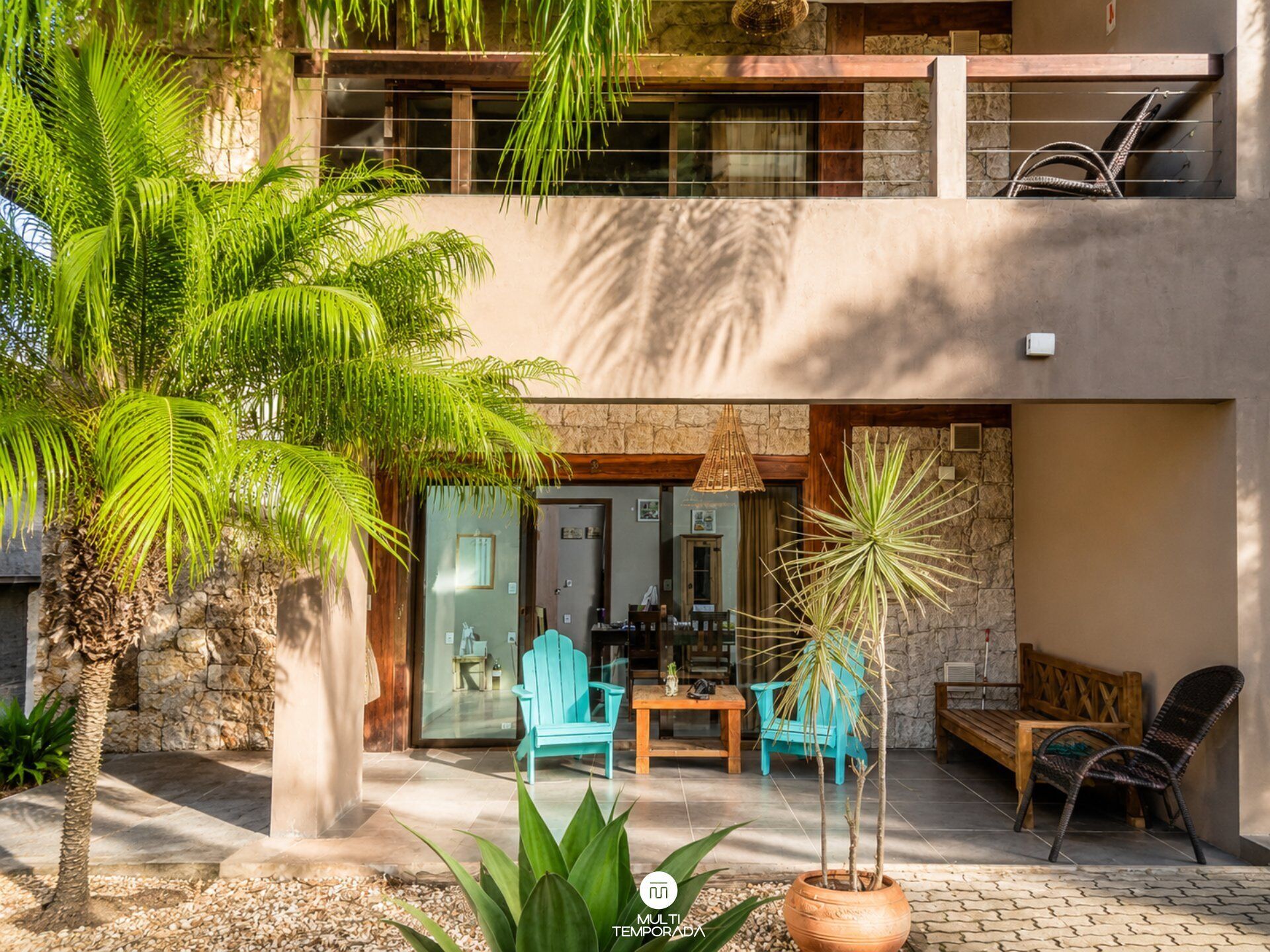 Un edificio de dos pisos con un patio que cuenta con mobiliario exterior, un muro de piedra y una palmera.