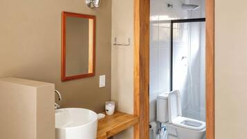 A bathroom with a wooden vanity, a large sink, a mirror, a toilet, and a shower enclosure.
