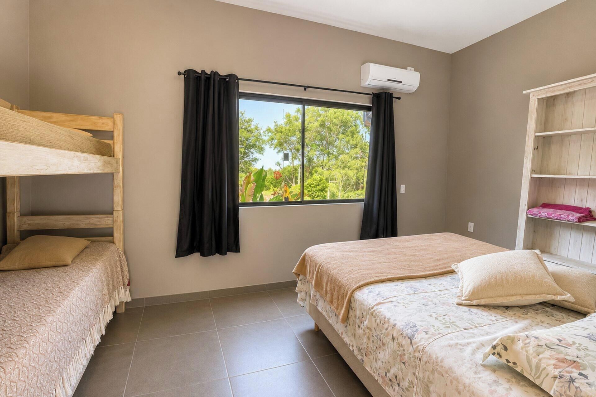 Un dormitorio con literas, una ventana con cortinas, una cama con colcha estampada y una estantería de madera.