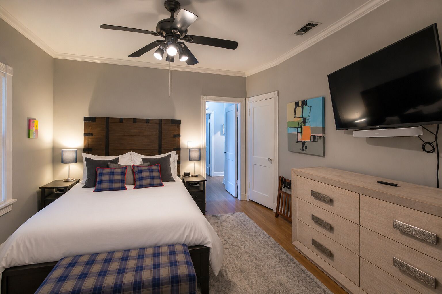 A bedroom with a bed, bedside tables, a ceiling fan, a television, and a door leading to another room.