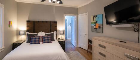 A bedroom with a bed, bedside tables, a ceiling fan, a television, and a door leading to another room.