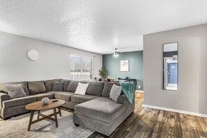A modern living room with a sectional sofa, a coffee table, and a dining area in the background.