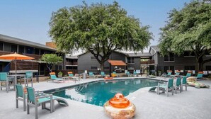Ein Swimmingpool mit Liegestühlen und Sonnenschirmen, umgeben von Bäumen und einem Gebäude.