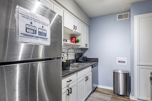A kitchen with stainless steel appliances, white cabinets, a sink, and a trash can.
