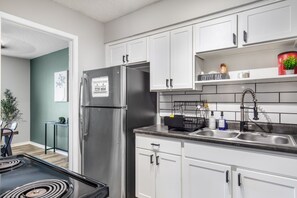 A modern kitchen with white cabinets, a stainless steel refrigerator, a black stove, and a coffee bar area.