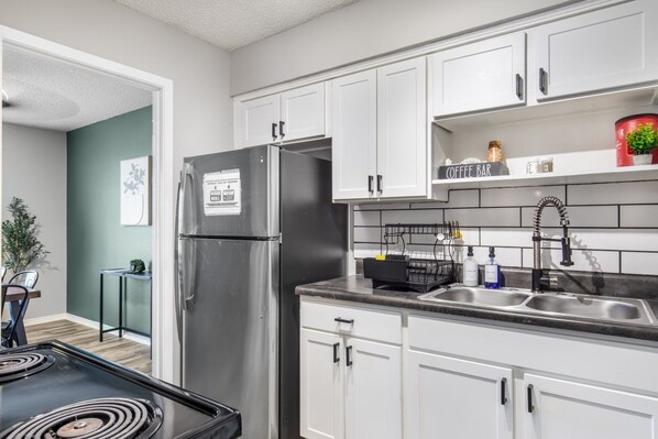 A modern kitchen with white cabinets, a stainless steel refrigerator, a black stove, and a coffee bar area.