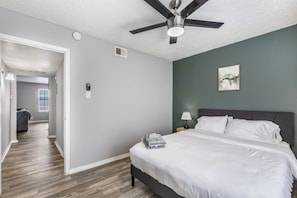 A bedroom with a bed, a ceiling fan, a nightstand, and a wall-mounted lamp.