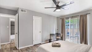 Ein Hotelzimmer mit Bett, Schreibtisch, Stuhl, Deckenventilator und Blick ins Freie.