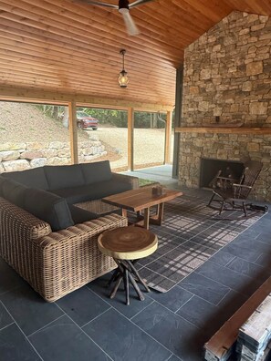 Eine überdachte Terrasse mit Steinmauer, Kamin, Korbmöbeln und Blick ins Freie.