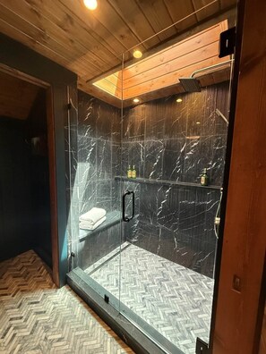 Ein Duschraum mit Glaswänden, einem Fußboden mit Fischgrätenmuster, einer Holzbalkendecke und einer Marmorwand.
