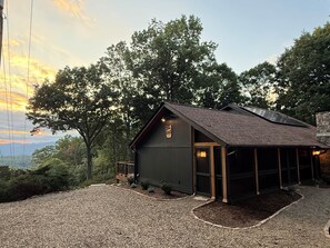 Eine Holzhütte mit Schotterauffahrt, einer Holzterrasse und Blick auf den umliegenden Wald.