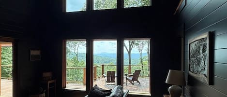 A cozy room with a leather sofa, a wooden table, and a view of the outdoors through large windows.