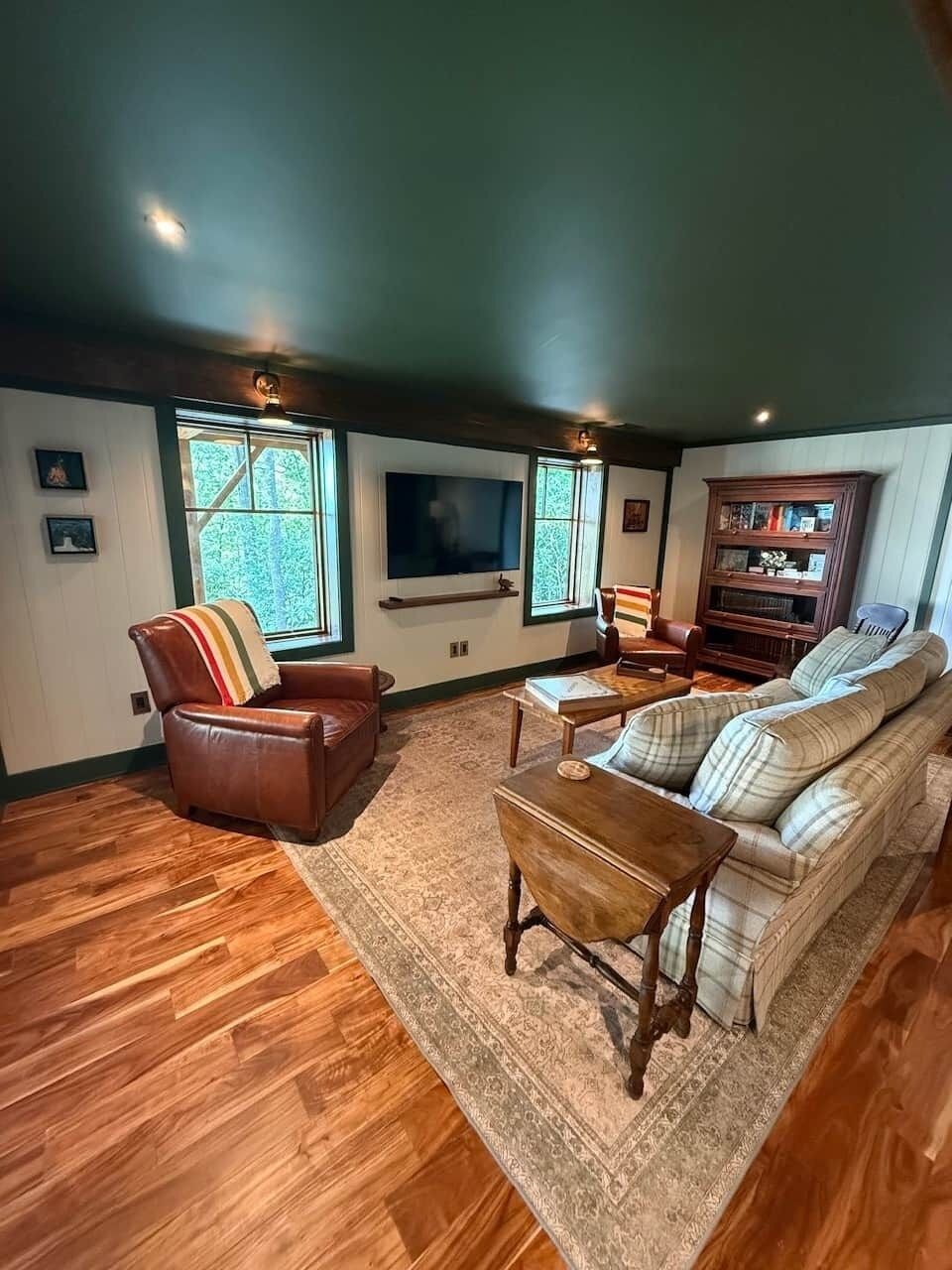A living room with a wooden floor, leather sofa, armchairs, a coffee table, and a television.